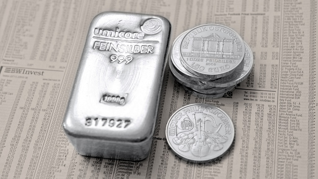 Ein 1 Kg Silber Barren und eine Wiener Philharmoniker Münze auf dem Wirtschaftsteil einer Zeitung liegend