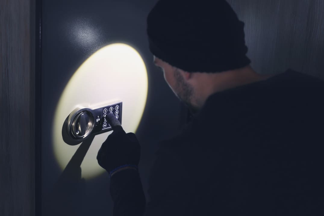 Un ladrón vestido de negro abre una caja fuerte a la luz de una linterna