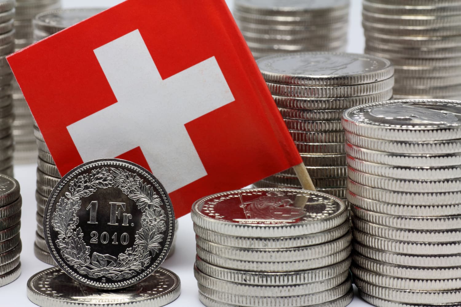 Schweizer Münzen gestapelt und eine Schweizerfahne.